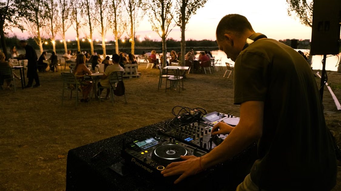 Een DJ draait bij zonsondergang voor een buitenfeest met lichtjes in de bomen